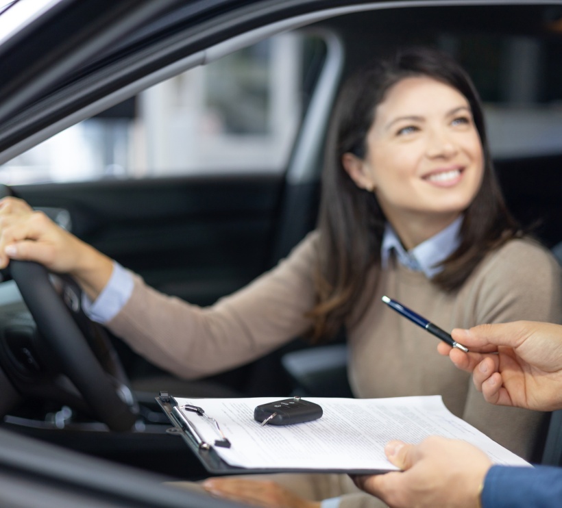 Szczęśliwa kobieta siedzi na miejscu kierowcy gotowa do podpisania umowy leasingu samochodu